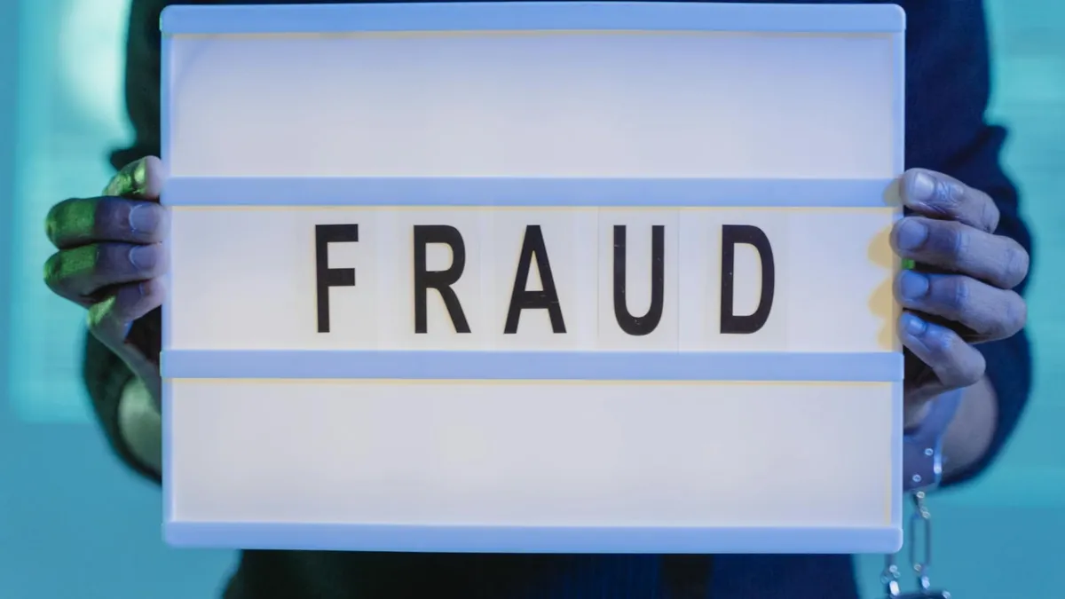 Close-up of hands holding a sign with 'fraud', illuminated in blue light.