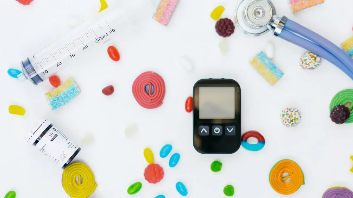 Flat lay of diabetes management tools and colorful candies on white background.