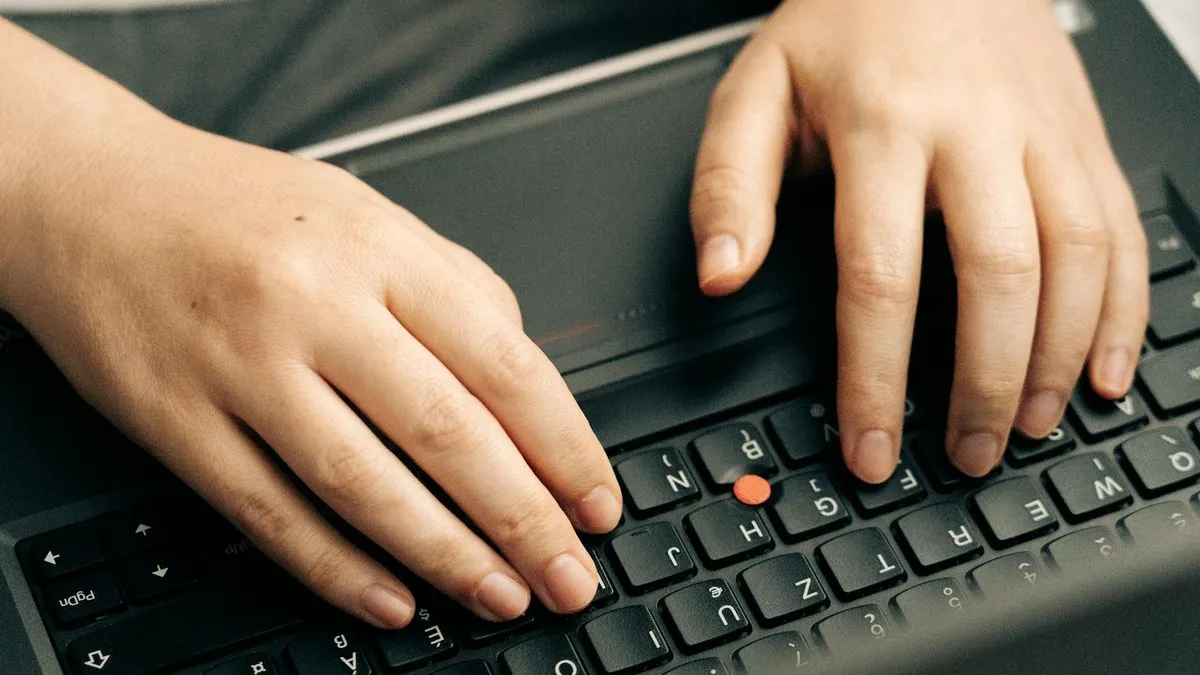Close-up of hands typing on a black laptop keyboard with a red trackpoint in the center.
