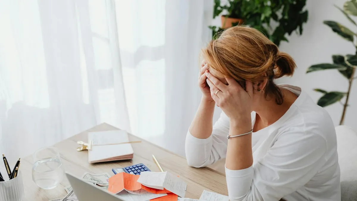 Woman stressed over financial receipts at a desk, dealing with expenses and calculations.