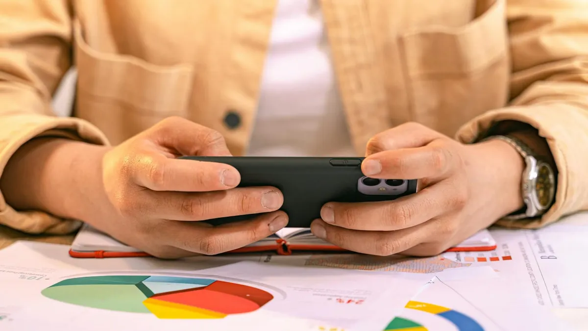 A business professional using a smartphone to analyze charts and graphs, likely for work.