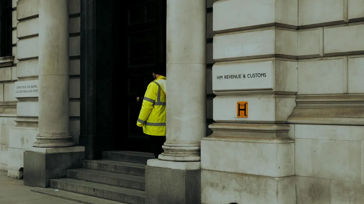A guard in yellow jacket at the entrance of HM Revenue & Customs building in the UK.