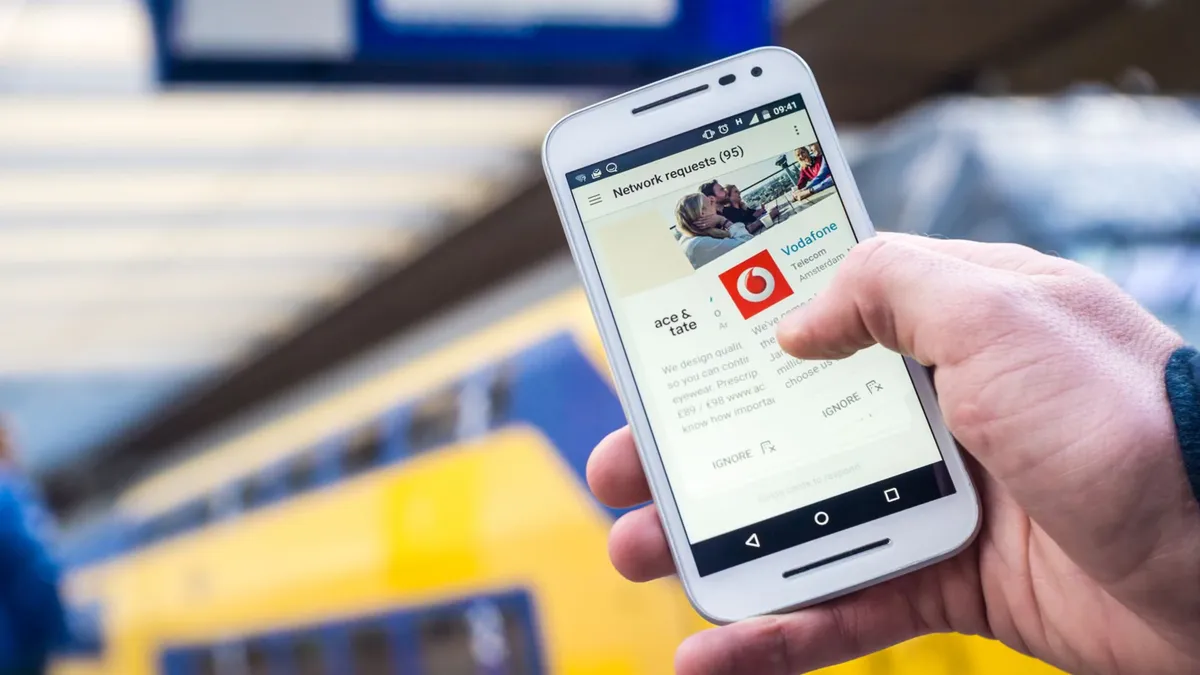 Close-up of a person using a smartphone with a train in the background, outdoors.