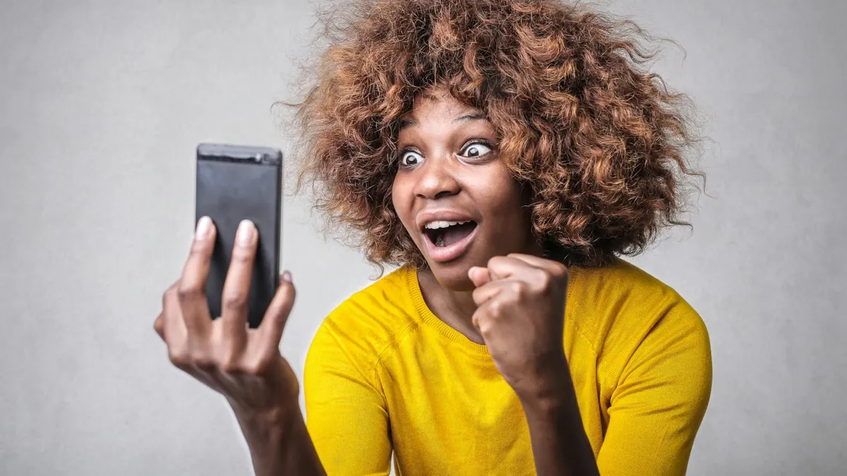 Joyful woman in yellow showing surprise and excitement at smartphone message indoors.