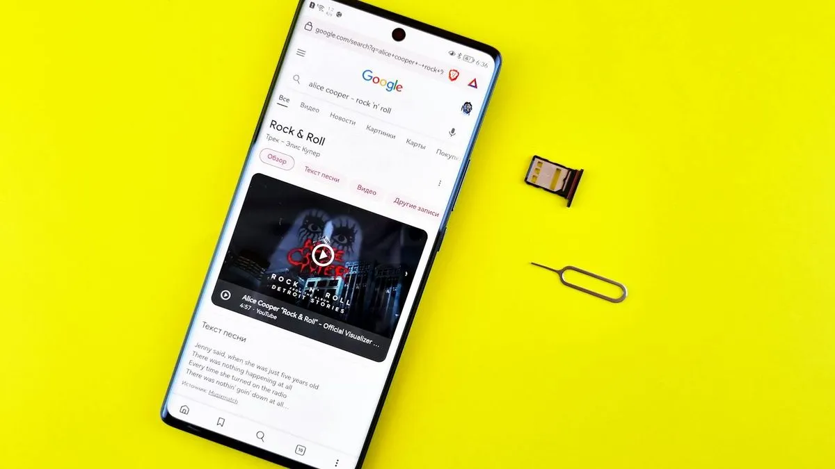 A smartphone on a yellow background with a SIM card tray and ejection tool next to it.