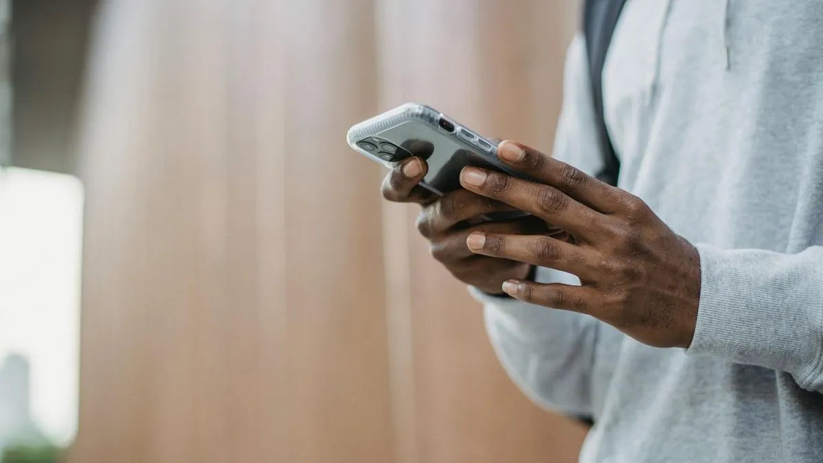 A person in a grey hoodie holds a smartphone, looking at the screen.