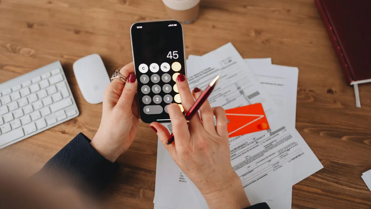 Hands using a calculator app on a smartphone over financial documents. Perfect for illustrating finance or technology themes.