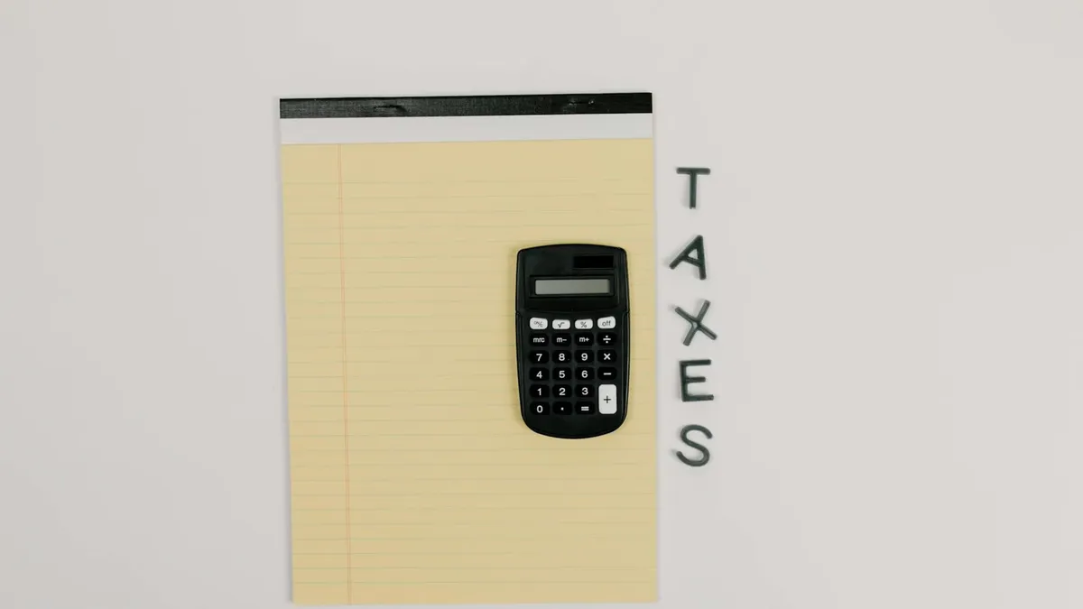 Top-down view of a calculator on a yellow notepad with 'TAXES' spelled out beside.