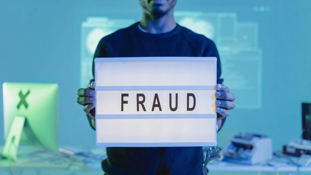 A man holding a sign reading 'FRAUD' in a tech environment, highlighting cybersecurity concerns.