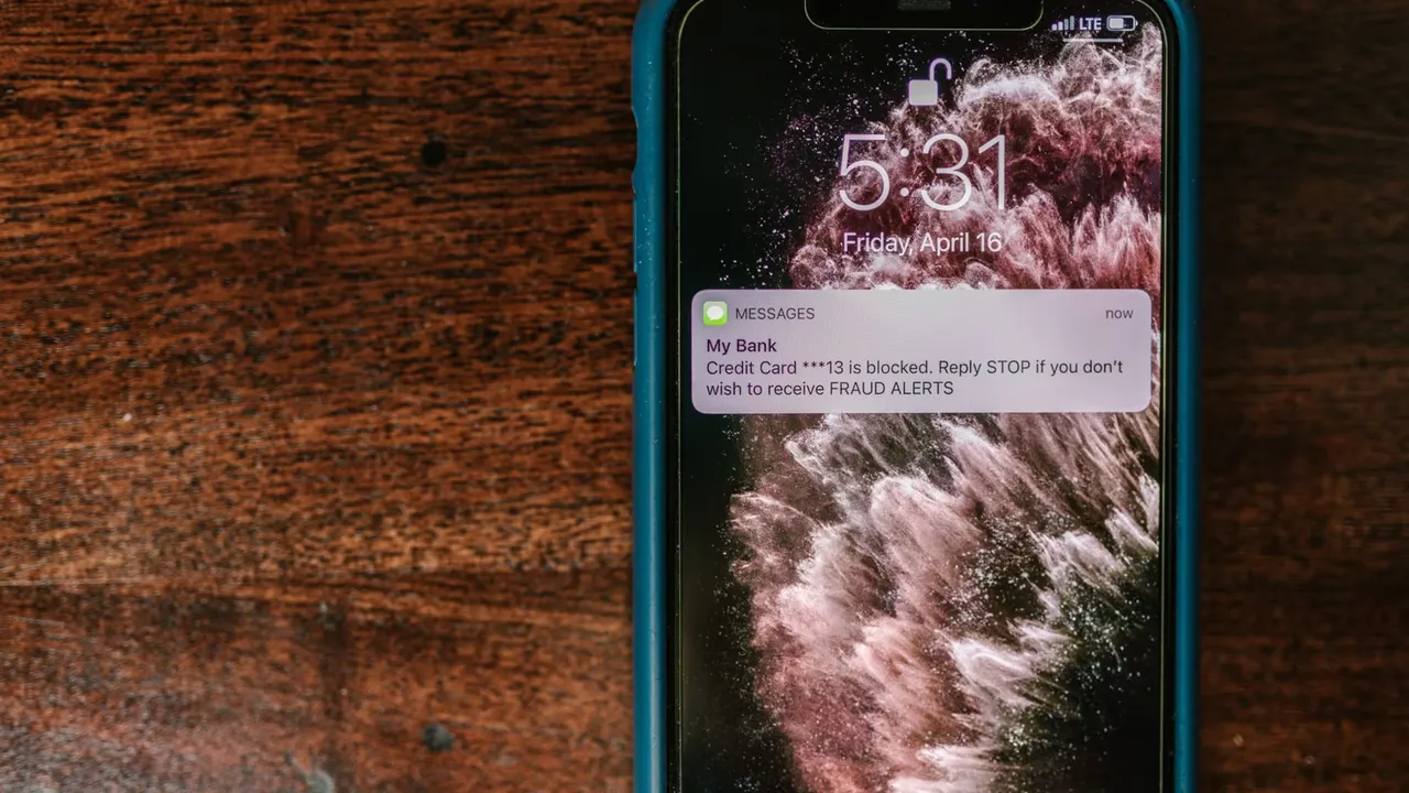 Close-up of smartphone displaying a fraud alert message on wooden surface.
