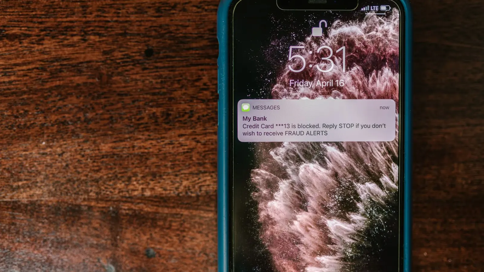 Close-up of smartphone displaying a fraud alert message on wooden surface.