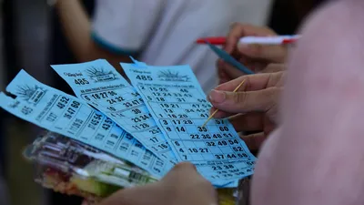 People playing bingo indoors, holding blue bingo cards with pen and markers.